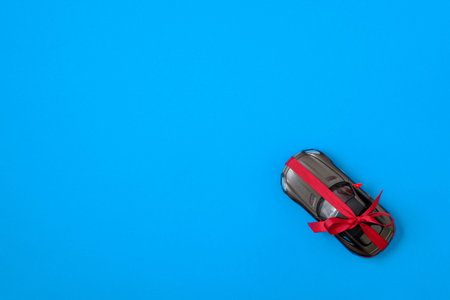 New modern car with red bow ribbon as a present. Toy car gift on blue background, flat lay composition. Top view.の写真素材