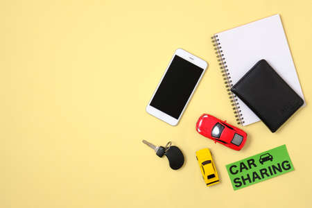 Car sharing concept. Toy cars, automobile key, driver license, blank notepad and smart phone on yellow background. Car sharing taxi service mockup, copy space, flat lay composition, top view.の写真素材
