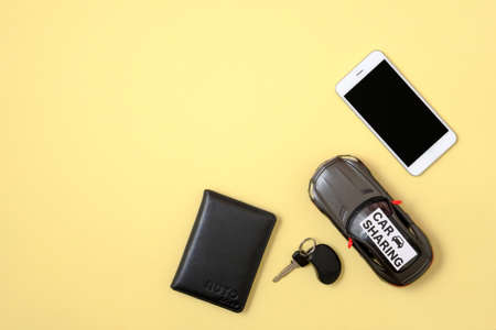 Carsharing concept. Toy car, car key, smart phone and driver license on yellow background. Minimal flat lay style composition, top view, copy space. Banner mockup for car rental agency.の写真素材