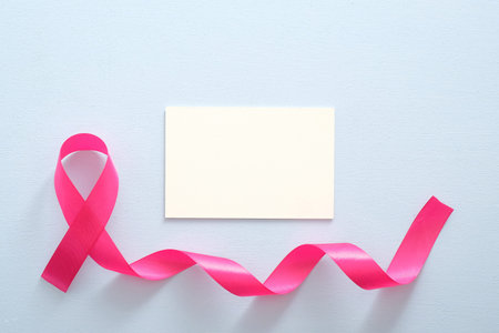 Breast cancer awareness month concept. Empty paper card mockup and pink breast cancer ribbon on blue...