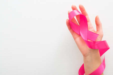 Female hand with pink ribbon as a symbol of the fight against breast cancer over white background. Breast cancer awareness month concept.の写真素材