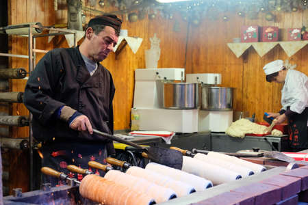 Budapest, Hungary. December 16, 2019: Vendor baking Trdelnik or Kurtosh cakes on the advent Christmas street market in Budapest, Hungaryのeditorial素材