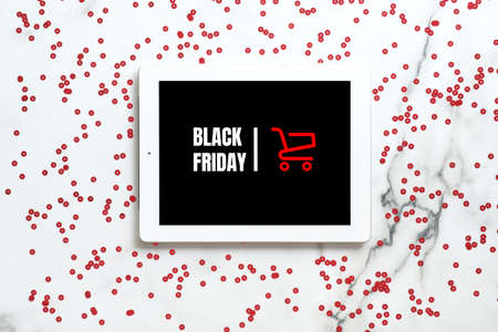 Black friday sale concept. Tablet pad with shopping card and text sign "Black friday" on screen over marble background with red confettiの写真素材