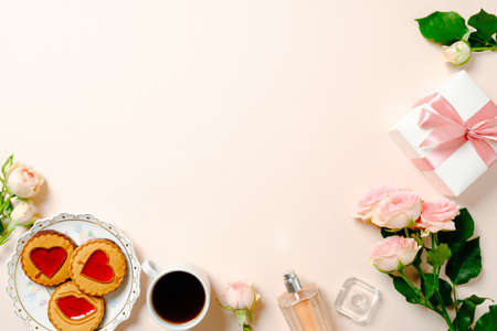 Frame made of biscuits, coffee cup, roses flowers bouquet, gift box. Flat lay women's desk table. Top view feminine background.の写真素材