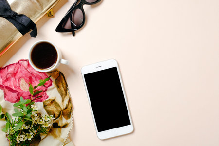 Flat lay home office desk. Female workspace with smartphone, pink scarf, golden accessories, coffee cup and sunglasses on pastel pink background. Top view feminine background with copy space for text.の写真素材