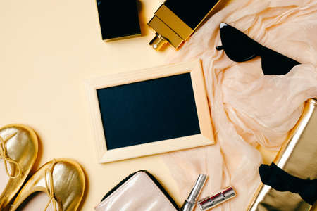 Female accessories set on beige background. Photo frame, sunglasses, golden summer slippers, cosmetic bag, perfume bottle. Womens desk with modern clothes. Fashion blogger stuff, flat lay, top view.の写真素材