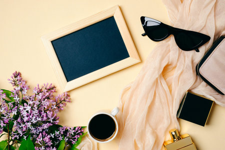 Female workspace with photo frame, sunglasses, silk scarf, coffee cup, accessories, perfume bottle, lilac flowers on beige background. Flat lay women's office desk. Top view feminine background.の写真素材