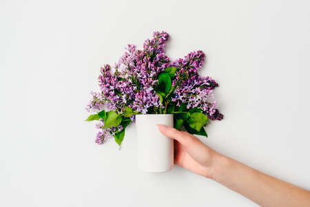 Female hand holding bouquet of lilacs flowers in modern glass vase on gray background. Flat lay composition in minimalist style, top view, overhead. Spring flowers concept.の写真素材