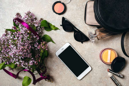 Flat lay modern minimal home workspace desk with lilac flowers, sunglasses, smartphone, leather bag, wallet, woman cosmetic, perfume on concrete background. Top view feminine stuff, fashion blog heroの写真素材