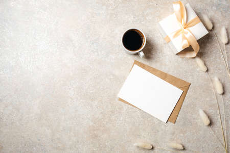 Minimal home office desk workspace with blank paper card, kraft envelope, coffee cup, gift box, dry flowers. Flat lay, top view social media hero header background.の写真素材