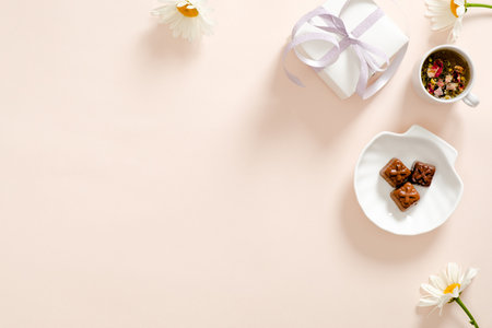 Romantic flatlay composition with gift box, herbal tea, ribbon, daisy chamomile flower on pastel...