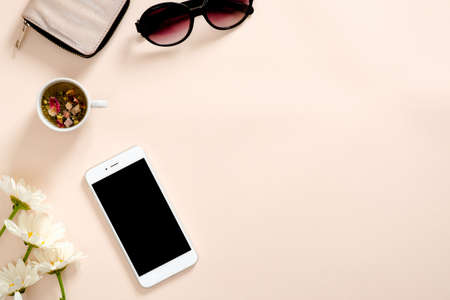Flatlay composition with feminine accessories, tea cup, smartphone blank screen mockup, sunglasses, daisy flowers on pastel pink background. Feminine home office desk concept. Flat lay, top viewの写真素材