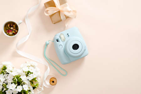 Modern instant camera, daisy flowers, cup of tea, gift box, ribbon on pastel pink background. Flat lay, top view, overhead. Fashion blogger workspace, beauty and technology concept.の写真素材