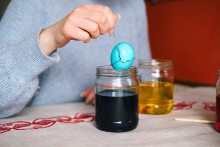 Female hand dyeing easter egg on blue liquid. Preparation to celebrate easter, easter eggs painting.