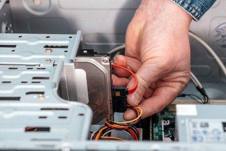 Hand of man plugging SATA (Serial AT Attachment, Serial ATA) data cable in hard drive device....