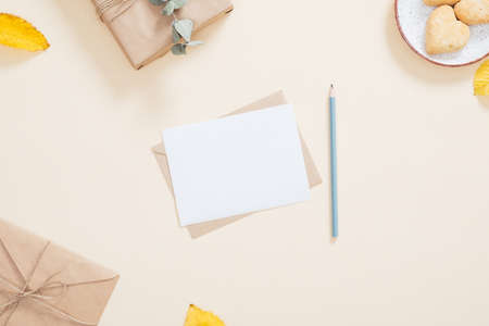Autumn composition. Letter, blank paper card, fallen leaves, gift box, cookies on pastel beige background. Autumn, fall concept. Flat lay, top view, overhead.のeditorial素材