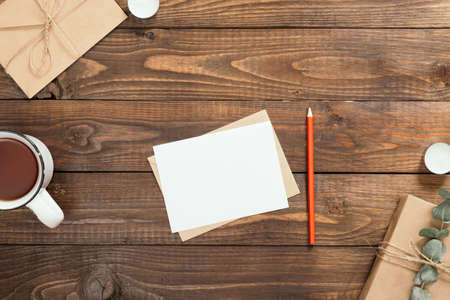 Autumn flatlay composition with letter, blank paper card, cup of tea, gift box, envelope, candles on wooden background. Cozy autumn or winter holiday concept. Flat lay, top viewの写真素材