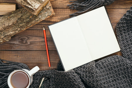 Hygge style flatlay composition with book, cup of coffee, fashion knitted scarf, firewood on wooden...