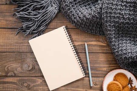 Flatlay autumn composition. Women fashion scarf, paper notepad with empty page, pen, cookies on wooden background. Flat lay, top view, overhead. Cozy home desk, hygge, autumn fall conceptの写真素材
