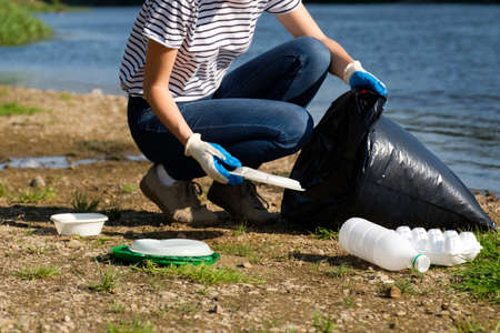 Volunteer woman collecting plastic garbage on coast of the river. Cleaning environment conceptの写真素材