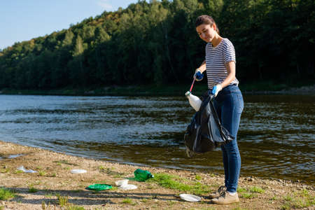 Volunteer woman picking up plastic garbage on the beach. Cleaning environment conceptの写真素材