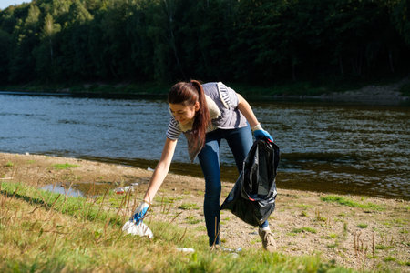Volunteer woman collecting plastic rubbish on coast of the river. Cleaning environment concept