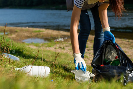 Volunteer woman collecting plastic rubbish on coast of the river. Cleaning environment concept