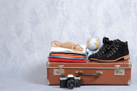 Retro leather suitcase with travel accessories on gray background. Stack of clothes, film photo camera, suede shoes, globe. Travel concept, banner mockup with copy spaceの写真素材