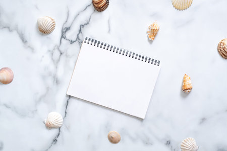 Sea shells and blank paper notepad with copy space for your text on marble background. Summer...