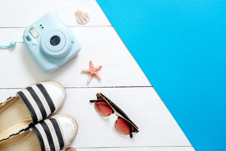 Instant camera, striped sandals, vintage glasses, seashells and starfish on white wooden background. Accessories and clothing of tourist, fashion blogger, hipster. Summer holiday vacation conceptの写真素材