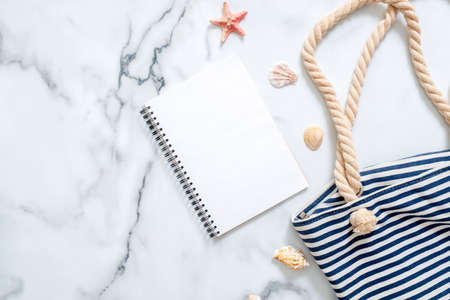 Blank notepad, striped summer bag, seashells on marble background. Women's desk of traveler, beauty blogger, digital nomad, hipster girl. Summer holiday, vacation, sea resort, journey conceptの写真素材