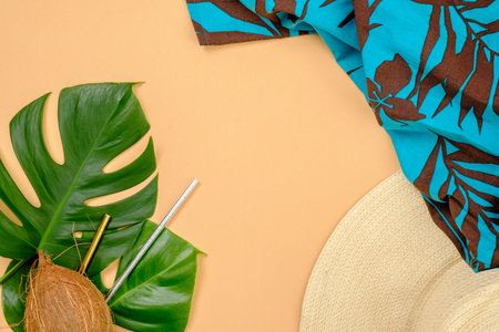 Tropical monstera leaves, coconut, drinking straws, straw hat and blue feminine dress on yellow...