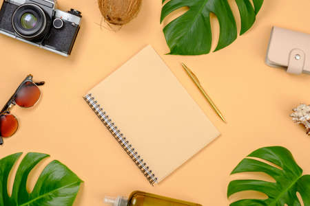 Flat lay traveler accessories on yellow background with copy space. Top view paper notepad, tropical monstera leaves, coconut, sunglasses, purse, suntan lotion, essential oil. Travel vacation conceptの写真素材