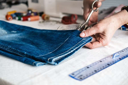 Tailor cutting jeans with scissors at workshopの写真素材