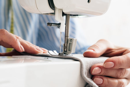 Close-up partial view of seamstress working with sewing machine and textile fabric at atelier...