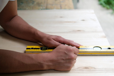 Carpenter marking straight line on plywood sheet using spirit level in carpentry workshop....
