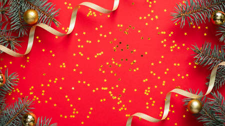 Christmas frame border. Fir tree branches decorated gold balls and ribbon, golden confetti stars on red background. Christmas, winter holiday, New Year celebration concept. Greeting card mockup.の写真素材