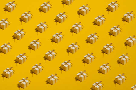 Pattern of white gift boxes with golden ribbon bow on yellow background. Christmas surprises, birthday presents concept.の写真素材