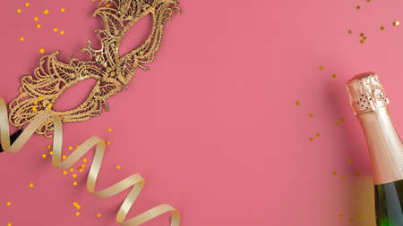 Christmas party background with champagne bottle, carnival mask, golden Christmas decorations, ribbon, confetti. Flat lay, top view.の写真素材