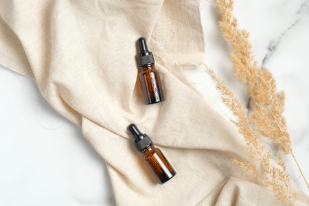 Amber glass essential oil brown bottles with beige fabric and dry flowers on marble background. Flat lay, top view. Natural organic beauty product packaging mockups.の写真素材