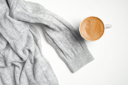 Knitted sweater and cup of coffee on white background. Autumn or winter composition. Cozy home desk,...