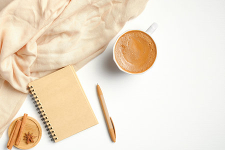 Cozy home desk with female beige scarf, cup of coffee, paper notebook, cinnamon sticks. Autumn or...