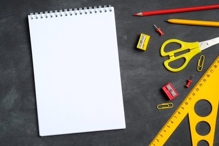 Blank paper notebook mockup and school stationery on black board background. Flat lay, top view,...