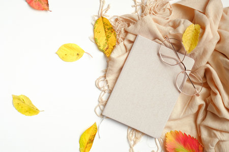 Autumn creative composition. Fallen leaves, paper notebook, women fashion glasses and beige scarf on...