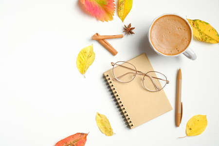 Flat lay autumn composition with cup of hot chocolate, paper notebook, fashion women glasses, cinnamon sticks, fallen leaves on white table. Top view, overhead. Cozy home feminine workspace concept.の写真素材