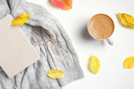 Autumn workspace with dried leaves, cup of coffee, female knitted sweater, glasses. Cozy, hygge,...