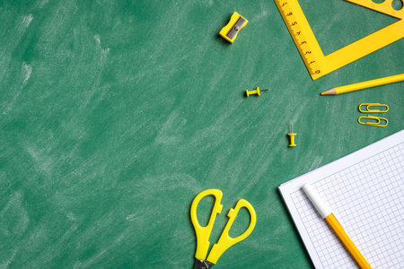 Back to school concept. Flat lay yellow school stationery and paper notebook on green chalkboard....