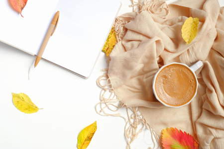Feminine workspace with fallen leaves, beige scarf, cup of coffee, paper notebook. Autumn desk...