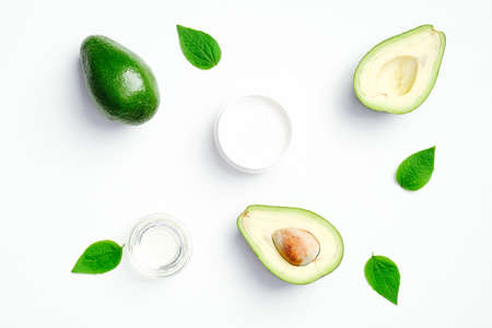 Flat lay composition with fresh ripe avocado and natural cream with green leaves on white background. SPA organic cosmetics for skin care, body treatmentの写真素材