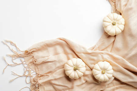 Elegant autumn composition. Small white pumpkins and beige scarf on white table. Autumn fashion concept.の写真素材